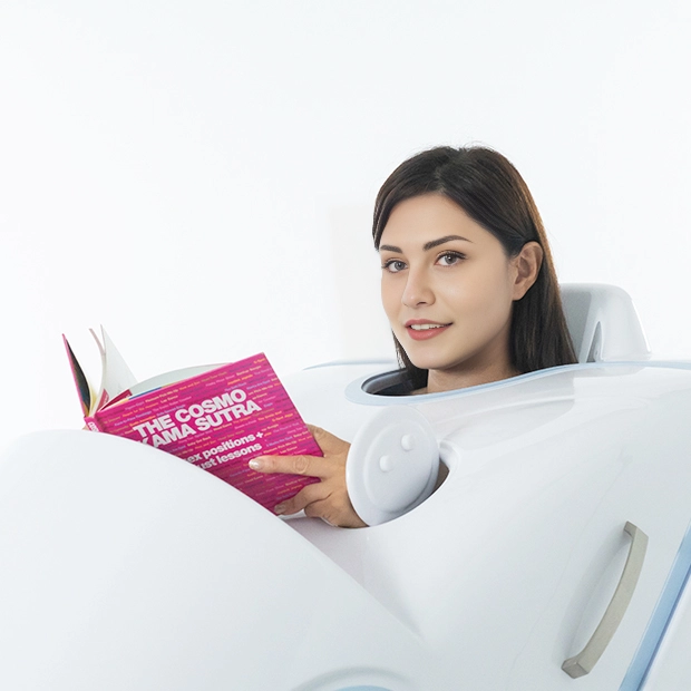 A woman relaxing inside the U-Mine BodyJet steam spa while comfortably reading a book, showcasing its open-door convenience feature.
